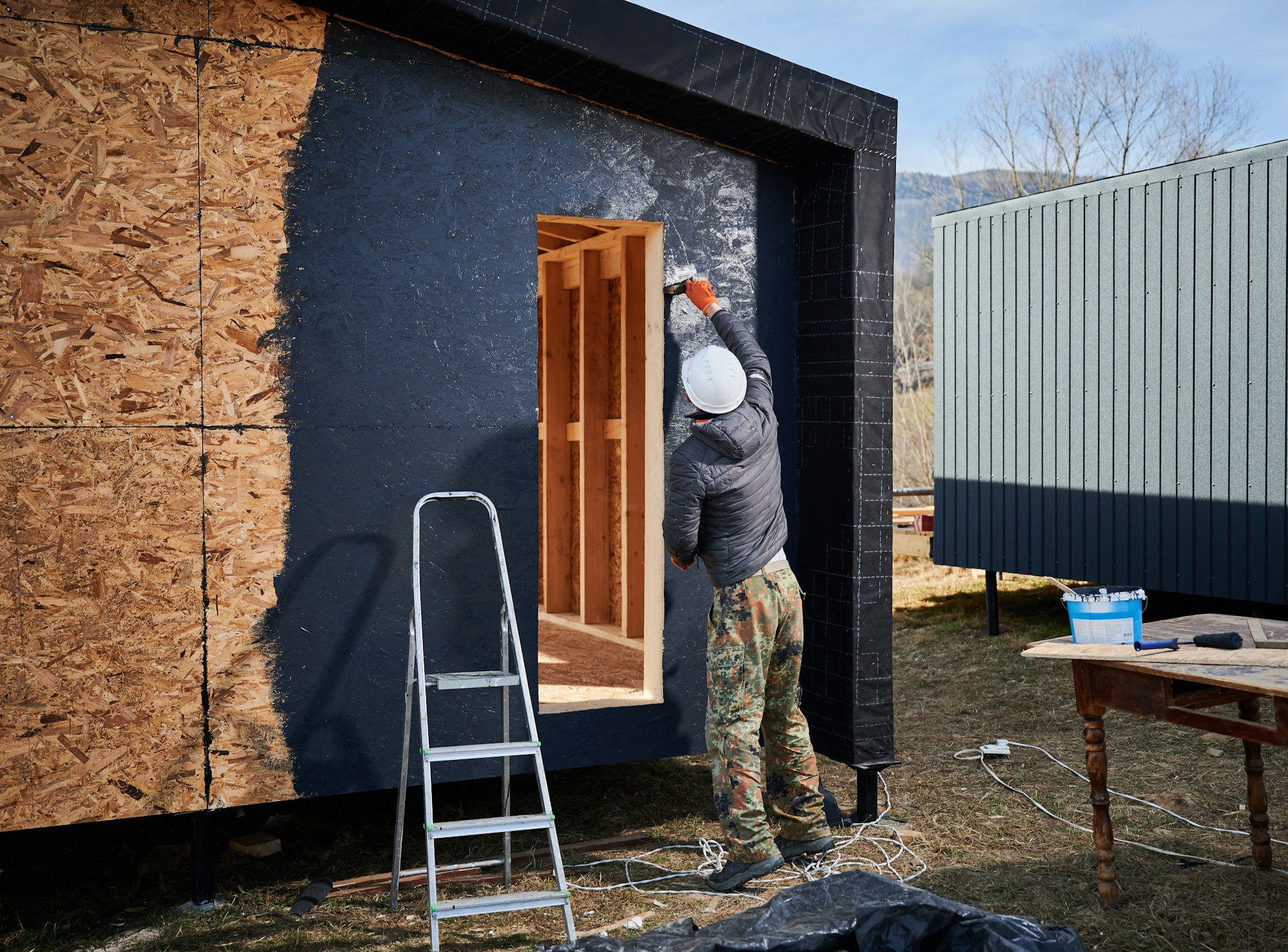 Male painter using paint roller, doing exterior paint work while building wooden frame house. Male painter using paint roller, doing exterior paint work while building wooden frame house.